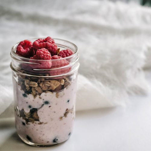 A photograph of overnight oats prepared in a jar and topped with raspberries