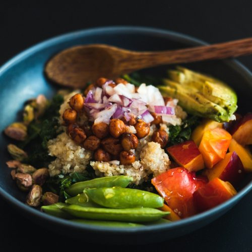 A photo of a bowl of quinoa topped with chopped onions, chickpeas, sliced avocado, sliced peach and mange tout